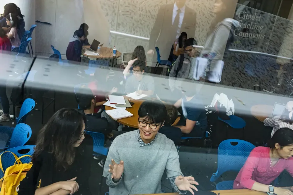 Looking through a window at students collaborating together in a common space.