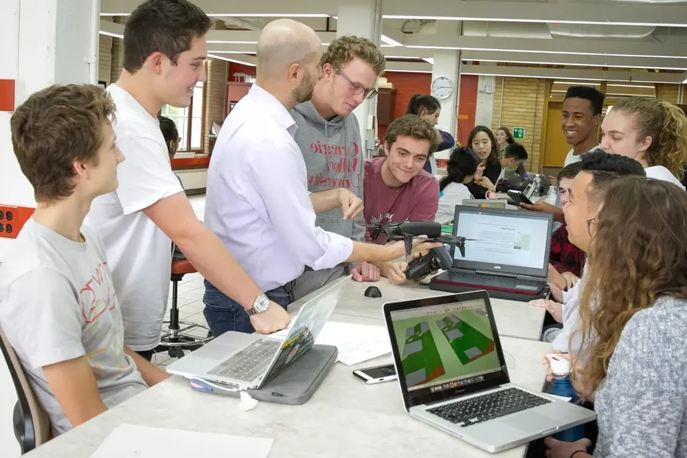 Students standing around a desk where a faculty member is showing a drone